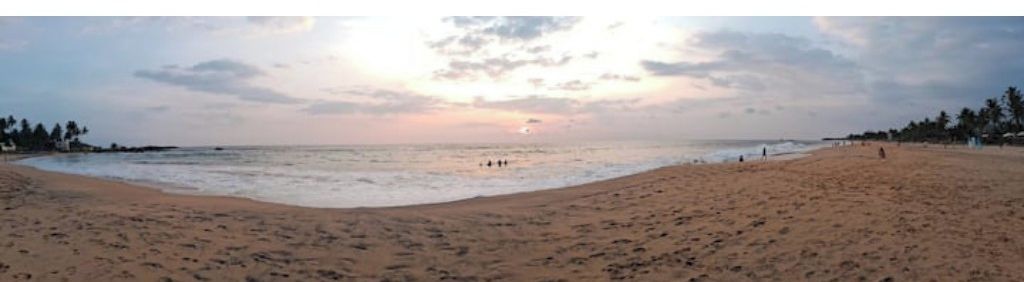 A wide beach with a calm sea and a sunset in the distance.