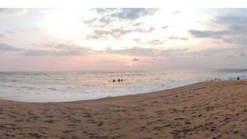A wide beach with a calm sea and a sunset in the distance.