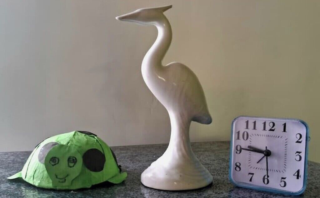 A ceramic bird sculpture and a clock on a countertop.