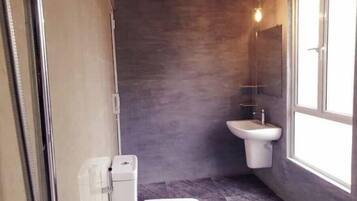 Un baño pequeño con inodoro blanco, lavamanos sobre pedestal y ventana que proporciona luz natural.