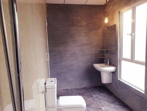 A compact bathroom with a white toilet, a pedestal sink, and a window providing natural light. - Villa in Hikkaduwa (Dodanduwa)
