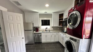 A compact kitchen with white cabinets, a stainless steel refrigerator, a dishwasher, a microwave, and a red washing machine.