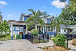 Ein zweistöckiges Haus mit Veranda, Garage und einem eingezäunten Garten mit Palmen.