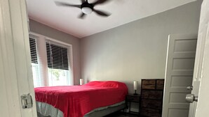 A bedroom with a bed, a ceiling fan, a dresser, and a door.