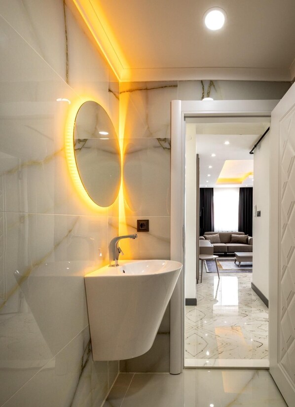 A modern bathroom with a white sink, a large mirror, and a marble wall. - selia suite (Trabzon)