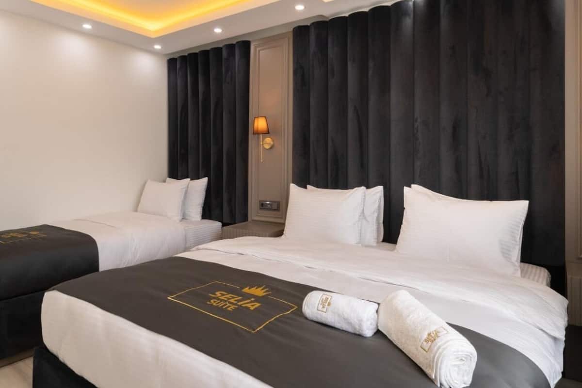 A modern hotel room with a large bed, two bedside tables, a dark headboard, and a ceiling light fixture.