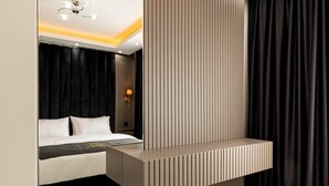 Ein modernes Hotelzimmer mit großem Spiegel, einem Bett mit weißer Bettwäsche, einem Nachttisch und einem an der Wand montierten Regal.