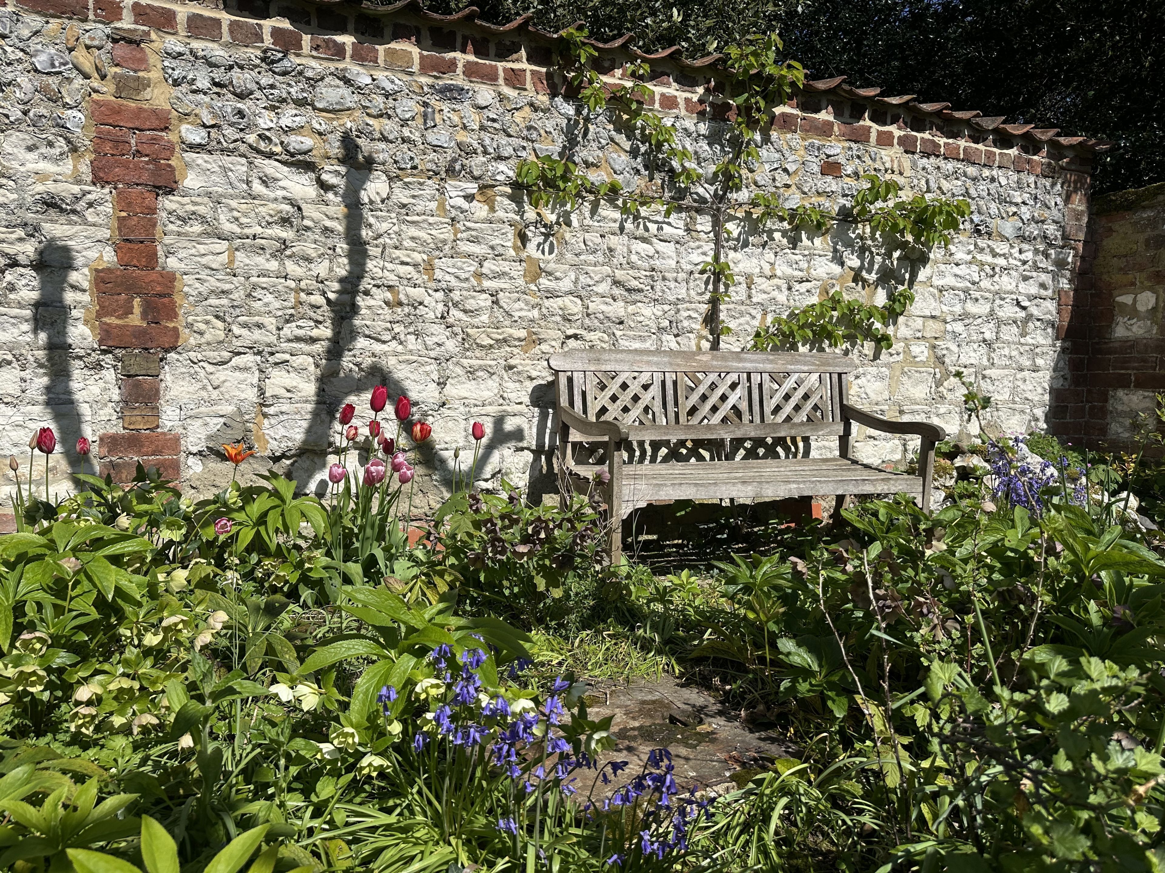 Eine Steinsäule mit einer hölzernen Bank in einem Garten.