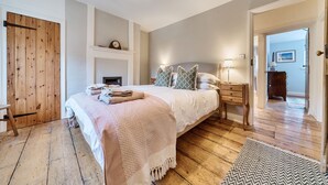 A bedroom with a wooden floor, a bed with a white and pink bedspread, a bedside table with a lamp, and a wooden wardrobe. - Ivy Cottage - sleeps 6 guests  in 3 bedrooms (Thornham)