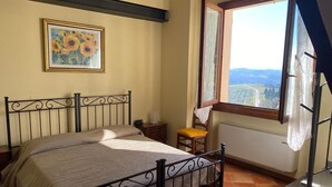 A bedroom with a bed, a window with a view, a painting on the wall, and a chair. - Suite Family Room with Attic and View, use of two pools at Casale del Vacanziere (Toscana)