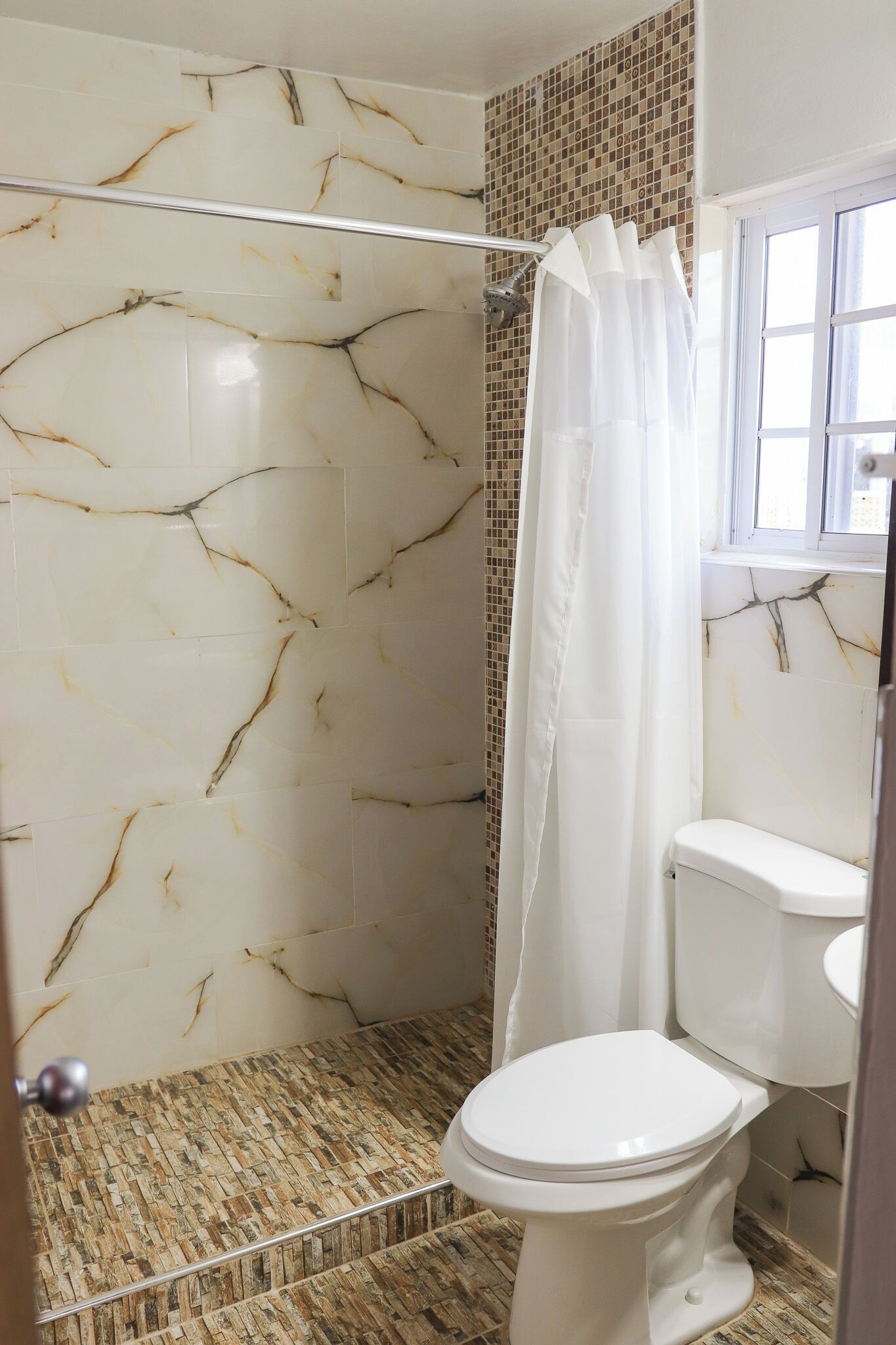 A bathroom with a shower, toilet, and a window.