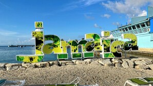 A beach with large letters spelling "Barbados" and a pier in the background.