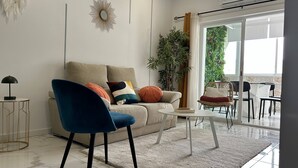 Un salón moderno con un sofá color beige, un sillón azul, una mesita blanca y una planta grande en maceta.