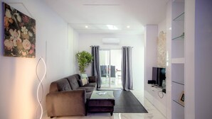 Un salón moderno con sofá, mesa de centro y televisor. Hay una planta y un cuadro en la pared.