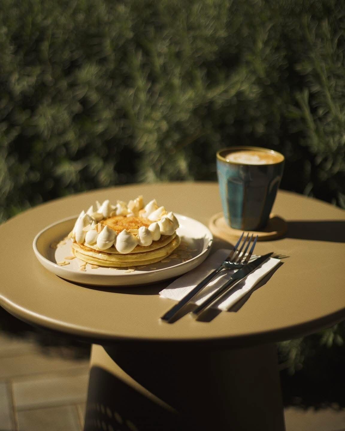 Una mesa con una pila de tortitas cubiertas de crema batida y una taza de café.