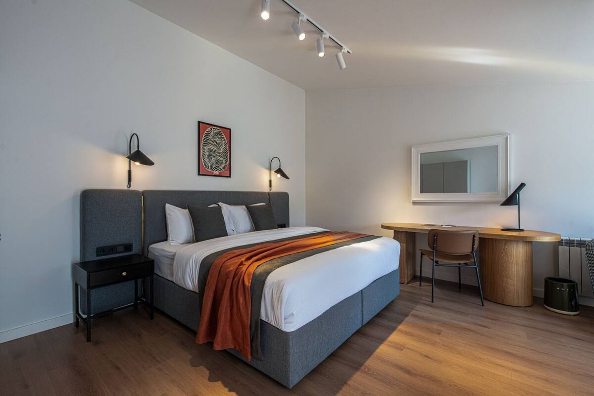 Ein modernes Hotelzimmer mit einem großen Bett, Nachttischen, einem Schreibtisch und einem Sessel.