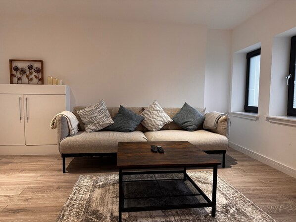 A living room with a beige sofa, patterned cushions, a wooden coffee table, and a rustic rug. - Ash Residence City Centre
A stunning warm and cozy city center apartment. (Aberdeen)