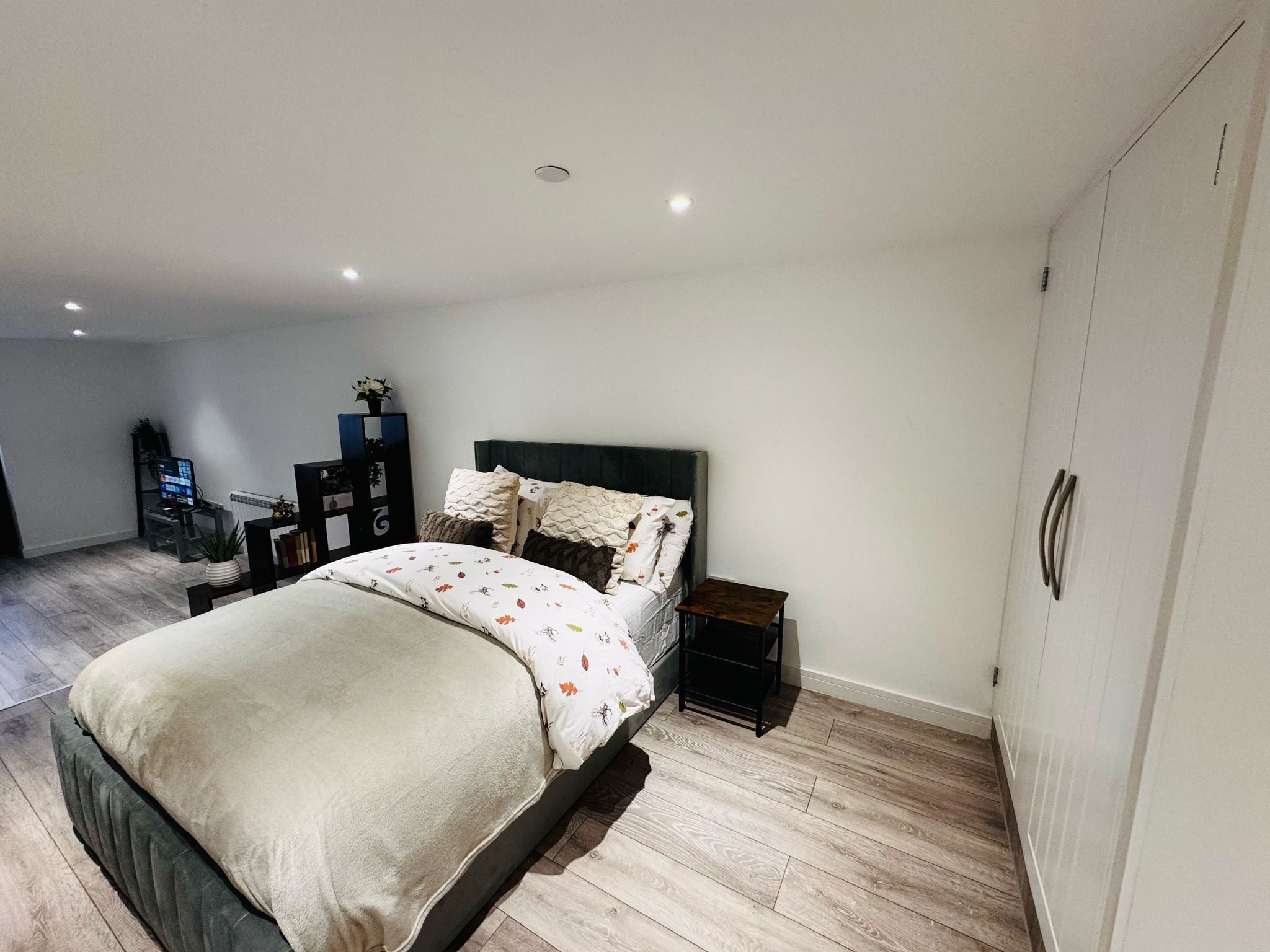 A modern bedroom with a bed, bedside tables, a TV, and a wardrobe.