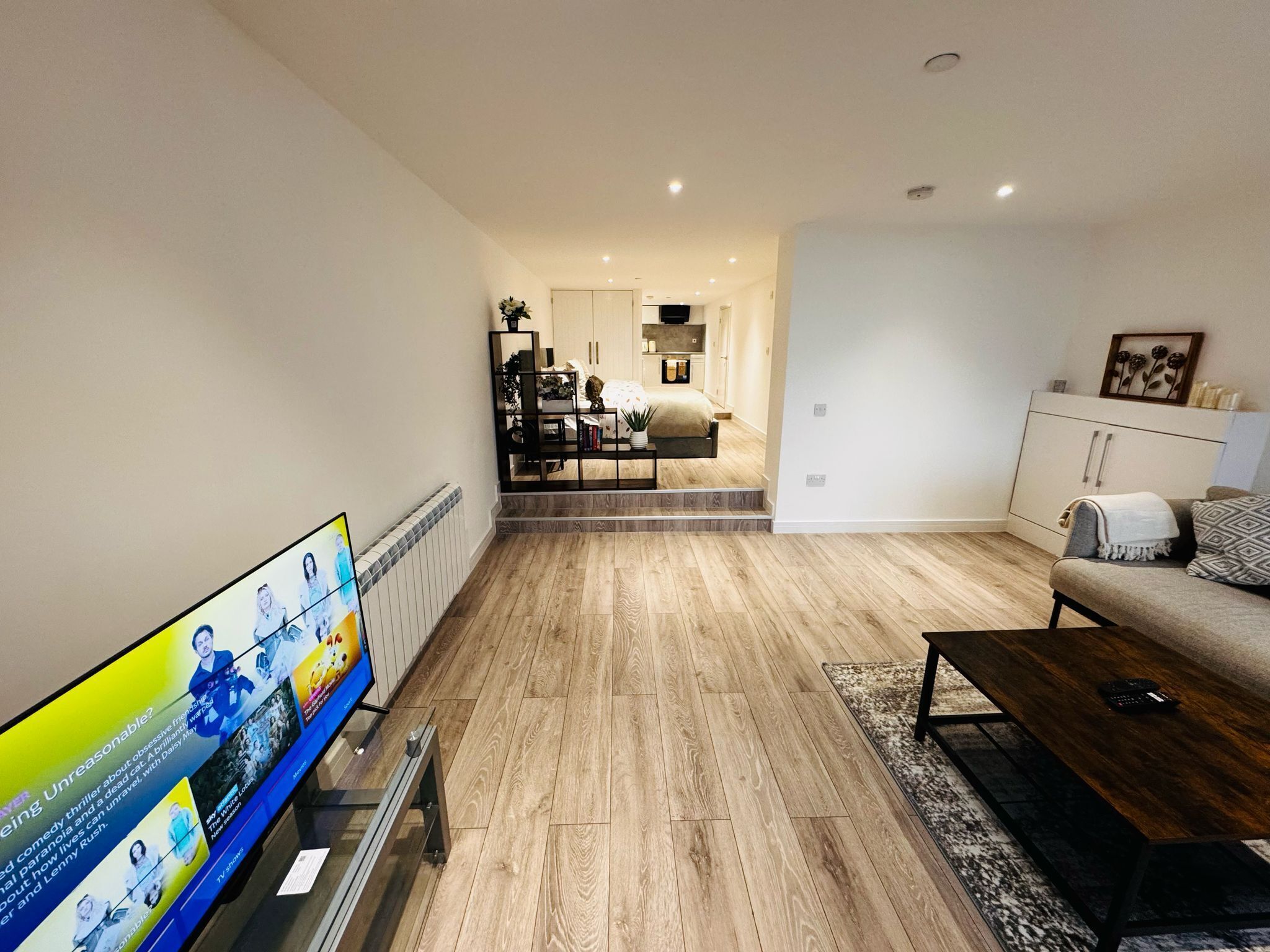 Een moderne woonkamer met een flatscreen televisie, een bank, een salontafel en een eethoek met een keuken op de achtergrond.