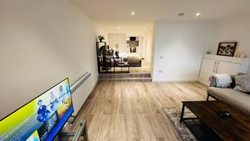 Een moderne woonkamer met een flatscreen televisie, een bank, een salontafel en een eethoek met een keuken op de achtergrond.