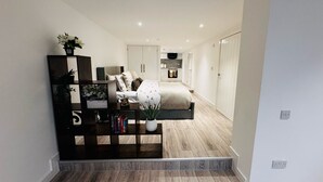 Ein modernes Schlafzimmer mit einem großen Bett, einem Nachttisch mit Büchern, einer kleinen Topfpflanze und einem Beistelltisch.