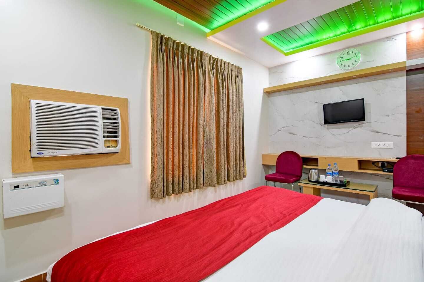 A hotel room with a bed, a TV, a desk with a chair, and a window with curtains.
