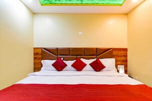 A neatly made bed with white linens and red pillows, a wooden headboard, and a green ceiling light.