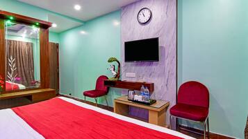 Habitación de hotel con una cama grande, dos sillas rojas, una mesita con un televisor y un reloj en la pared.