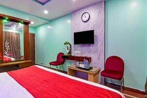 Habitación de hotel con una cama grande, dos sillas rojas, una mesita con un televisor y un reloj en la pared.