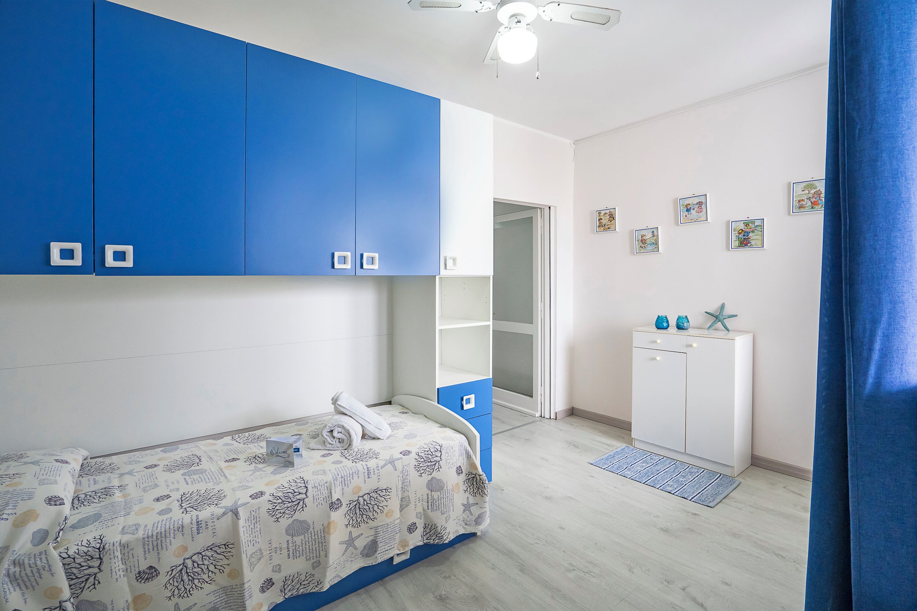 Quarto com cama, guarda-roupa, escrivaninha e porta que dá para outro cômodo.