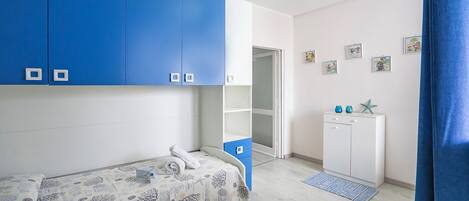 A bedroom with a bed, a wardrobe, a desk, and a door leading to another room.