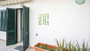 Eine weiße Wand mit grünen Fensterläden, ein Blumentopf und ein Schild mit grünem Text.