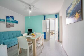 Un salon moderne avec un mur d’accent de couleur turquoise, un canapé blanc, une table à manger en verre et un ventilateur de plafond.