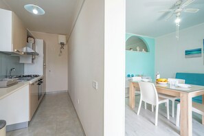 A modern kitchen with a stove, sink, and cabinets, a dining area with a table and chairs, and a ceiling fan. - Riva Di Mare Apartment Near The Sea (Porto Cesareo)
