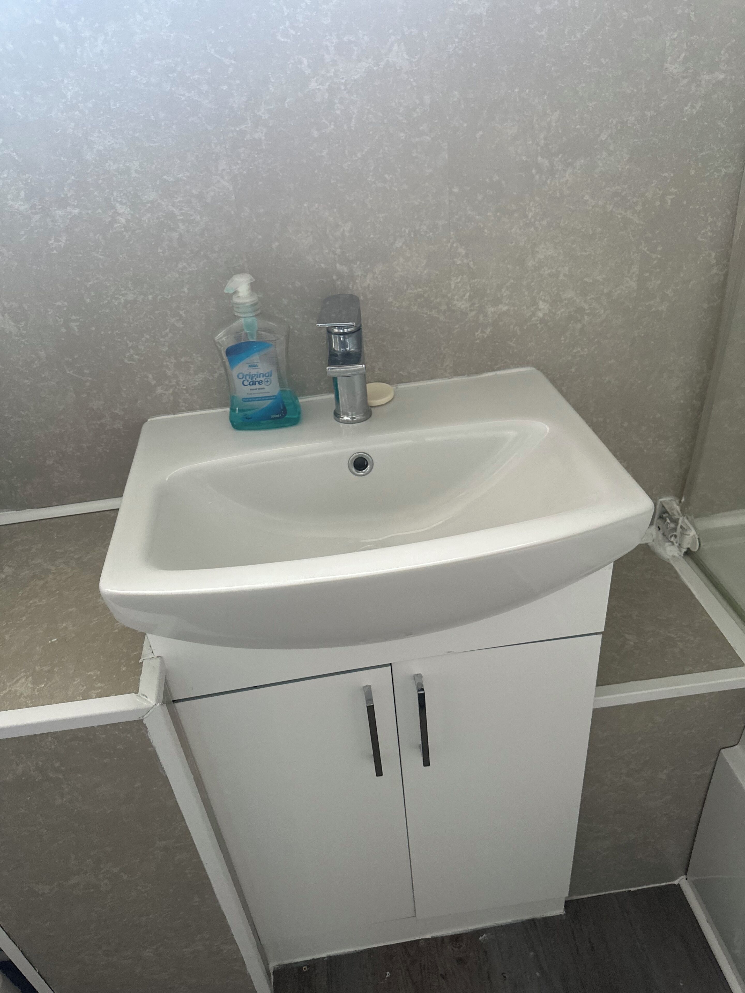 Een badkamer met een witte wastafel, een zeepdispenser en een kraan.