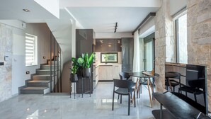 Een moderne keuken met een accentmuur van steen, een eethoek met een ronde tafel en stoelen, en een trap naar een verdieping.