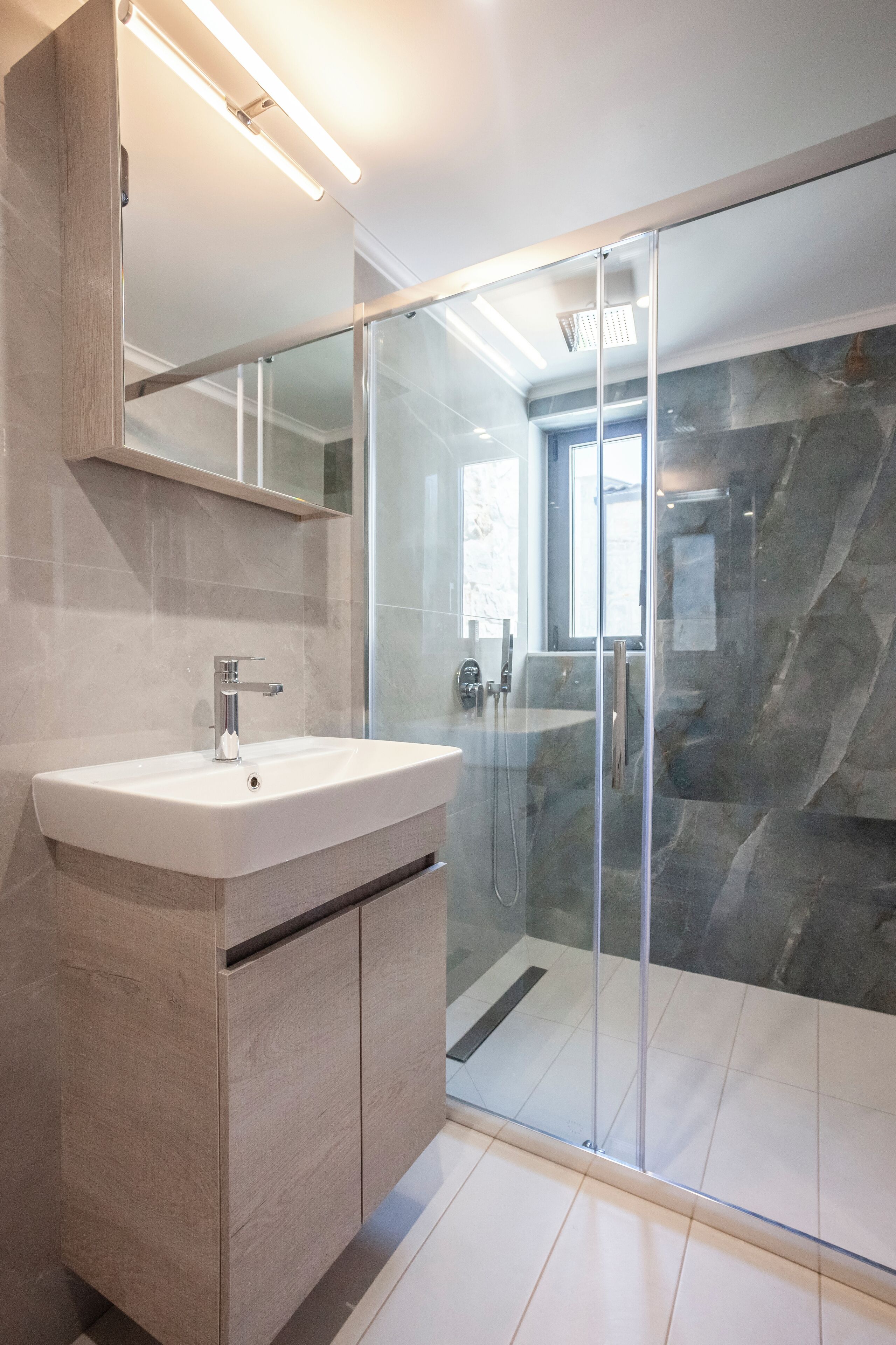 Een moderne badkamer met een douchecabine van glas, een wit wastafelmeubel en een houten opbergkast.