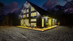 Une maison moderne dotée de grandes fenêtres, d’une cheminée et d’un porche bien éclairé.