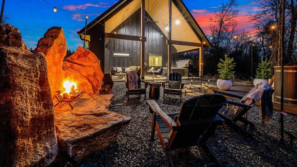 Un chalet rustique doté d’une grande véranda ouverte, d’un foyer en pierre et de coins salon extérieurs.