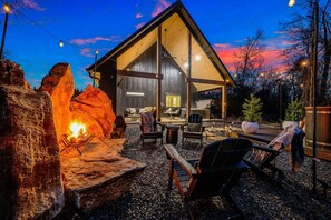 A rustic cabin with a large open porch, a stone fire pit, and outdoor seating. - Wellness Cabin Retreat: Hot Tub, Cold Plunge. Close to Casino & State Park/Lake (Broken Bow)