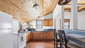 A kitchen with wooden cabinets, a white stove, and a dining area with a table and chairs. - Sunnyside Cottage (Cockburn Town)