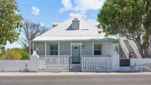 A white building with a green door and windows, labeled "Sunny Side," with a staircase leading to the roof. - Sunnyside Cottage (Cockburn Town)