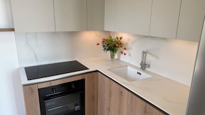 Uma cozinha com forno embutido, uma pia com torneira moderna e um vaso com flores na bancada.