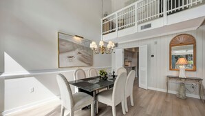 Un coin repas avec une table en marbre noir, des chaises à revêtement blanc, un lustre et un tableau accroché au mur.