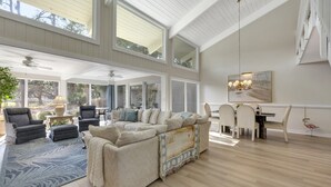 Un vaste espace de vie comprenant un grand canapé d’angle, une table à manger avec des chaises et un ventilateur de plafond.