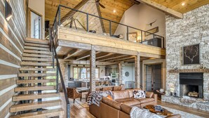 Ein großzügiger Wohnbereich mit hohen Decken, freiliegenden Holzbalken, einem Kamin aus Stein und einer gemütlichen Sitzecke mit einer Ledersofa und einer Treppe, die zu einer oberen Ebene führt.