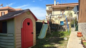 Uma casinha de brincar com uma porta vermelha e um escorrega num quintal.