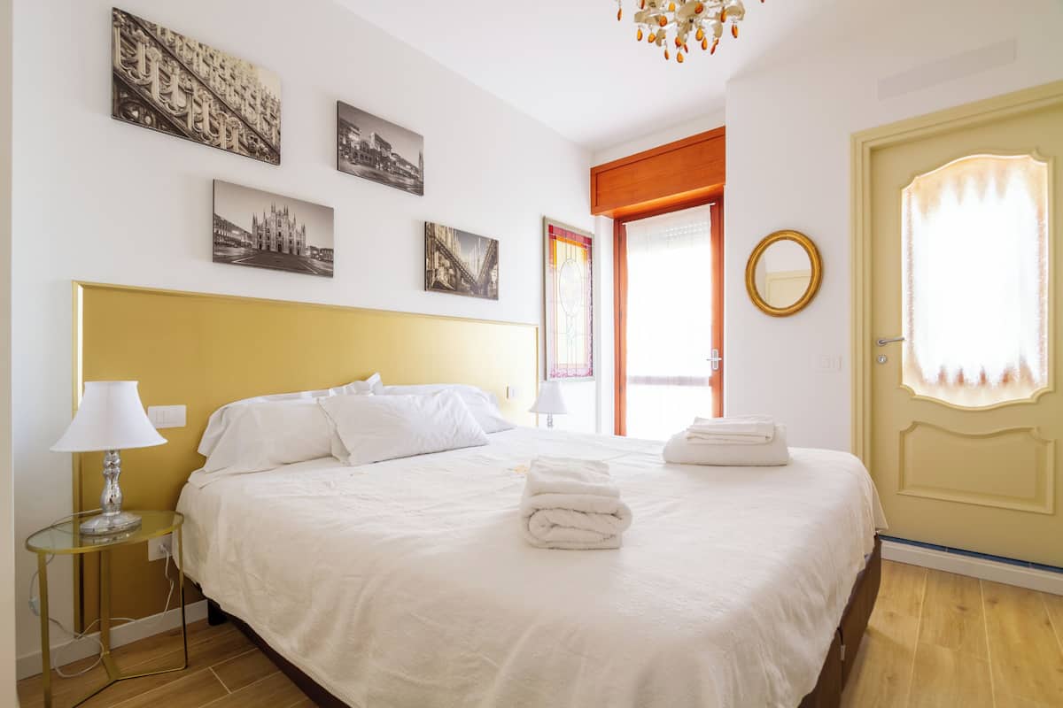 Una habitación de hotel con una cama grande, una mesita de noche con lámpara y una puerta con espejo.
