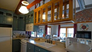 A kitchen with teal cabinets, a wooden upper cabinet, a white refrigerator, a stove, a sink, and a dining area with a table and chairs. - "City View " super cozy downtown Loft apartment (Bloomington)