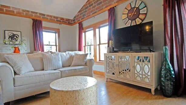 A living room with a sofa, a round coffee table, a TV on a cabinet, and a large clock on the wall. - "City View " super cozy downtown Loft apartment (Bloomington)